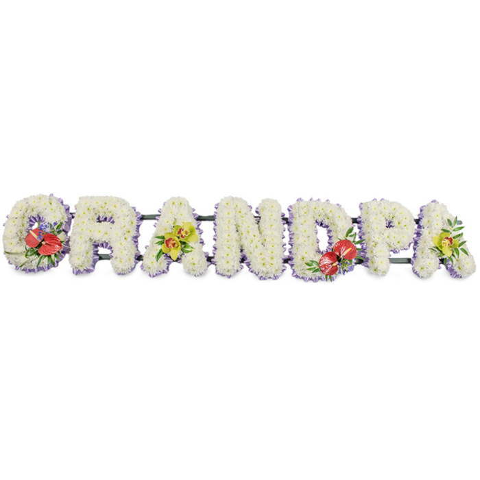 This image shows a dignified GRANDPA funeral tribute arranged in a long horizontal line, every letter large, bold, and crafted entirely from fresh flowers. The capital letters are built from tight clusters of white chrysanthemums, each small bloom nestled snugly next to the next, creating a thick, sumptuous layer of petals that feels soft and consoling. The bright white flowers stand out crisply against the plain white background, creating subtle shadows within the letters that emphasise their depth and three-dimensional form. A soft lavender ribbon trims the base of every letter, offering a gentle lilac border that defines the shapes and softens the overall look with a hint of cool colour. Dark green bars connect and support the letters beneath, glimpsed here and there between the blossoms and adding quiet structure. Along the word, exquisite accent sprays break the expanse of white with expressive symbolism: the 'G' and the 'D' are dressed with clusters of deep red anthuriums, their glossy, heart-like blooms and golden spadices arranged among lush green foliage and possibly small purple fillers, bringing intimacy and a sense of cherished memories. On the first 'A' and the last 'A', yellow-green orchids are arranged with equal care, their graceful, slightly exotic flowers and fresh greenery suggesting enduring love and gentle remembrance. This personalised tribute, just the sort of design families in Chessington might choose for a funeral or cremation service in the local area, captures the essence of a beloved grandfather's role-steady, loving, and central to family life-translated into carefully chosen and expertly arranged flowers.