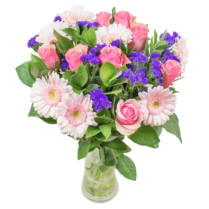 This lively, meticulously arranged bouquet stands in a pristine glass vase against a backdrop that emphasizes its fresh vibrancy. Around seven to nine pink roses-some gently furled, others beginning to open in classic spirals-form the centrepiece, reflecting timeless romance popular throughout Chessington homes. Five to seven pale pink gerbera daisies, with their broad, round heads and slightly lighter centers, surround the roses and lend a sense of spaciousness and light. Scattered throughout, vivid purple statice adds pops of colour and textural intrigue, their fine petals creating points of focus. The bouquet is set atop abundant, deep green foliage, drawing inspiration from nearby greenways like Chessington South's nature walks, evoking the scent and vitality of the local landscape. The entire arrangement is cradled in a sleek, transparent vase, where stems and water are clearly visible, symbolizing lasting freshness and a natural aesthetic. Ideal for birthdays, anniversaries, Mother's Day, or simply as an elegant decorative accent for local offices and homes along Moor Lane, this arrangement conveys Chessington's spirit of celebration and warm-heartedness.